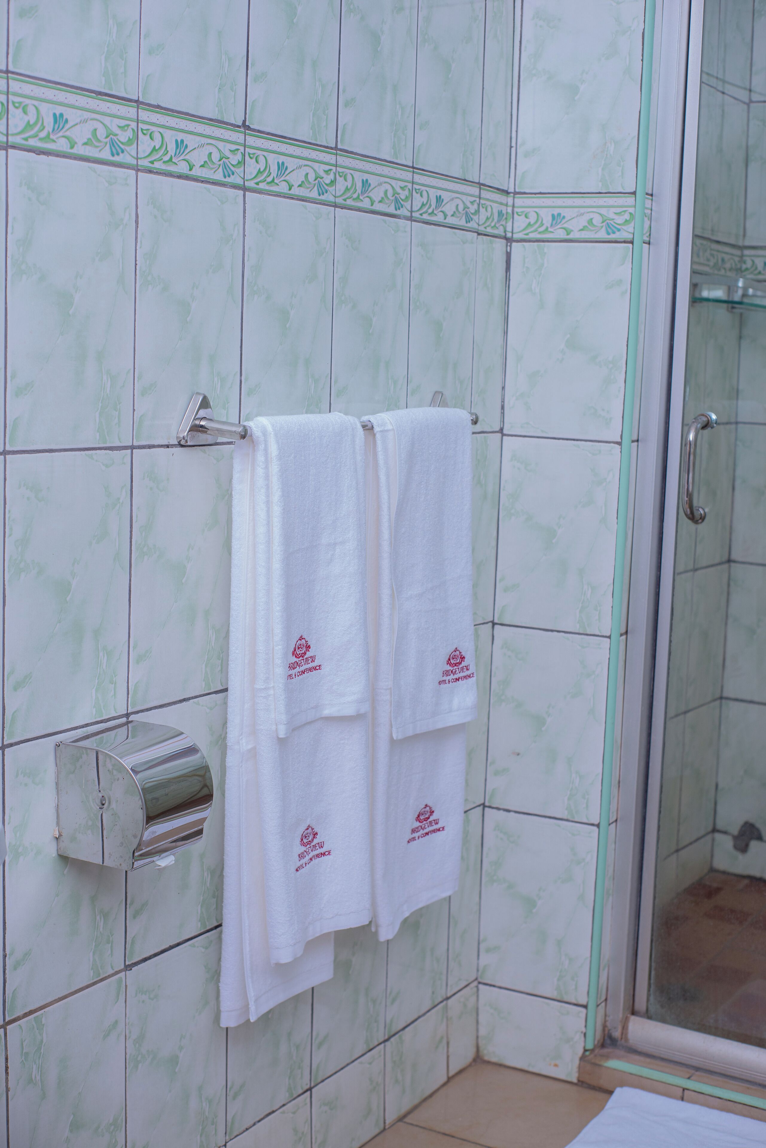 A bathroom with two white towels hanging on a rack, a towel dispenser, and a glass shower enclosure.