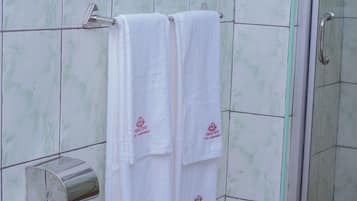 A bathroom with two white towels hanging on a rack, a towel dispenser, and a glass shower enclosure.