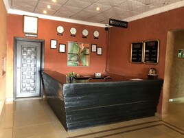 Un área de recepción con un mostrador negro, un cuadro abstracto enmarcado, relojes en la pared y un letrero que indica la recepción.