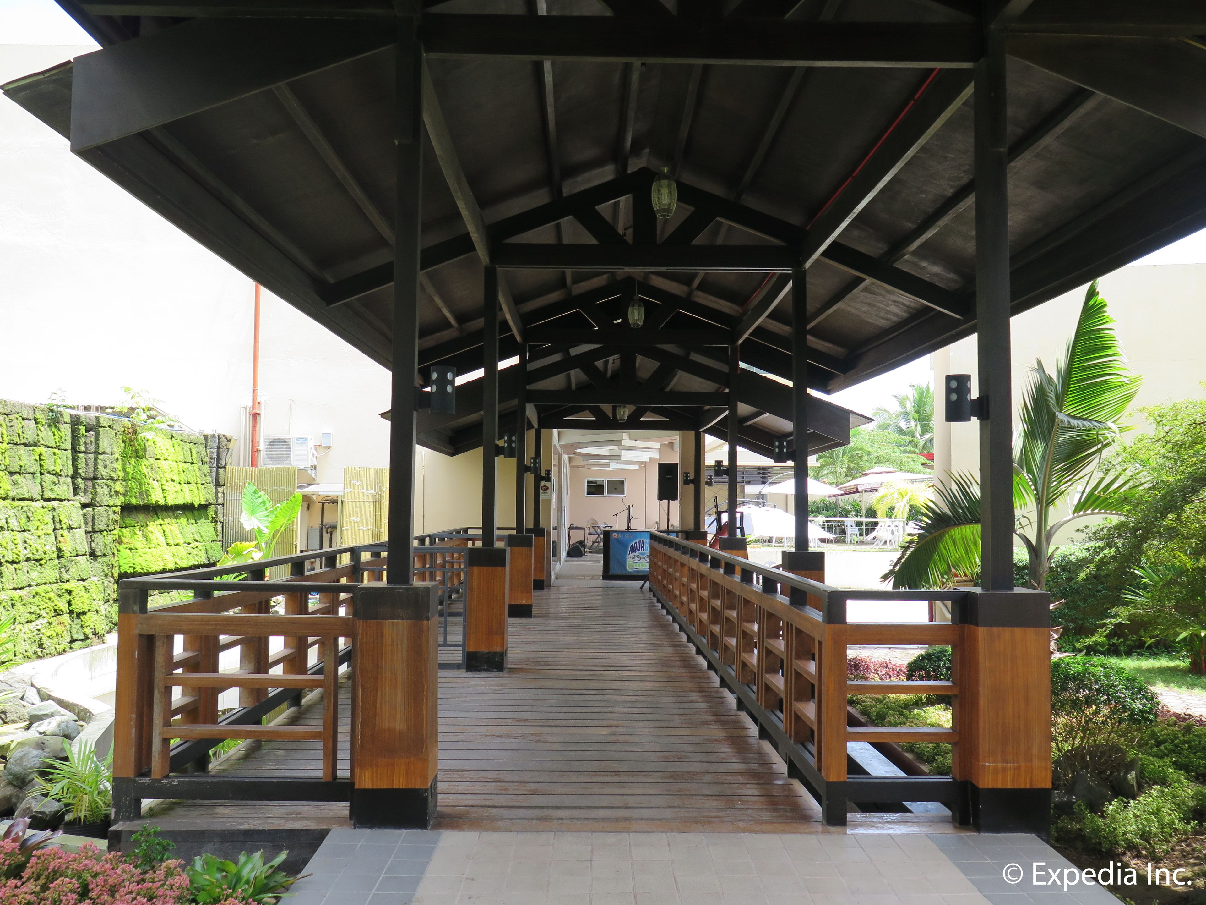 A covered walkway with wooden railings and a tiled floor, leading to a building entrance.