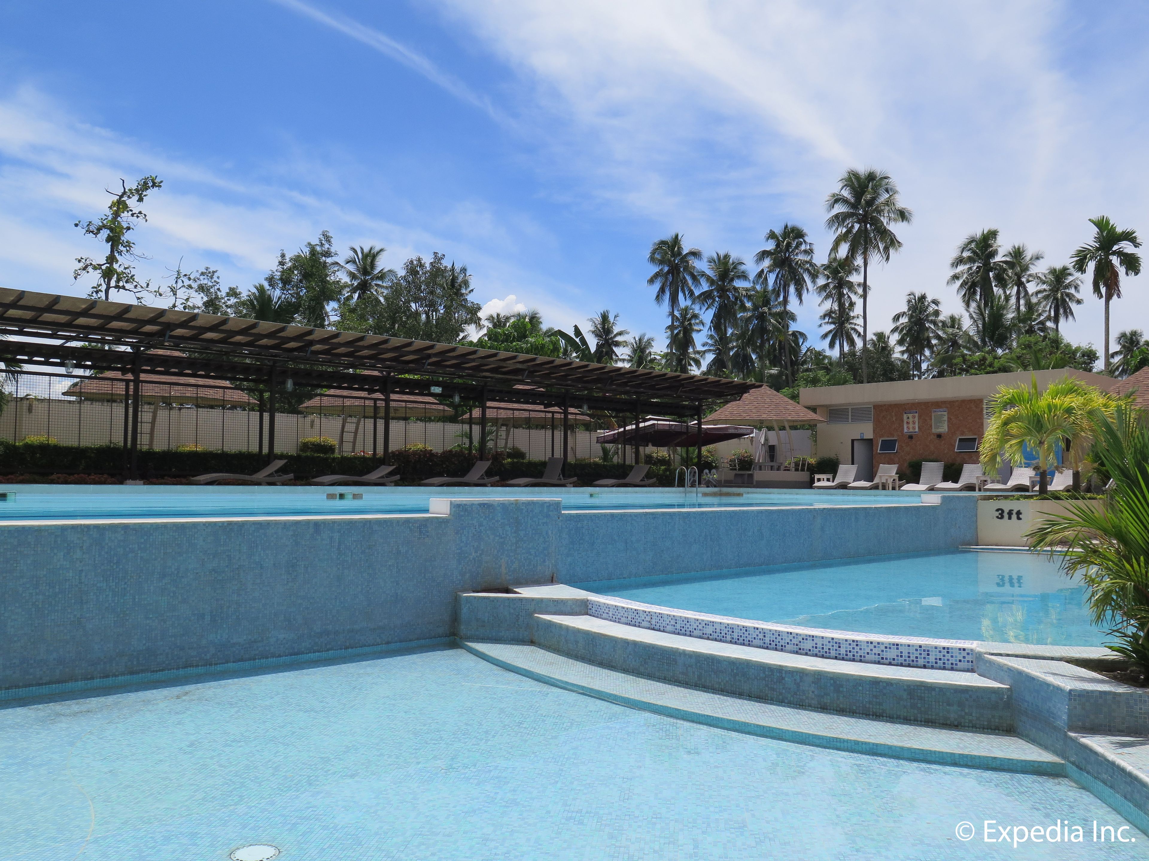 A swimming pool area with multiple pools, lounge chairs, and palm trees.