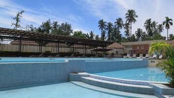 A swimming pool area with multiple pools, lounge chairs, and palm trees.