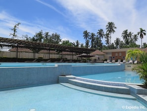 A swimming pool area with multiple pools, lounge chairs, and palm trees.