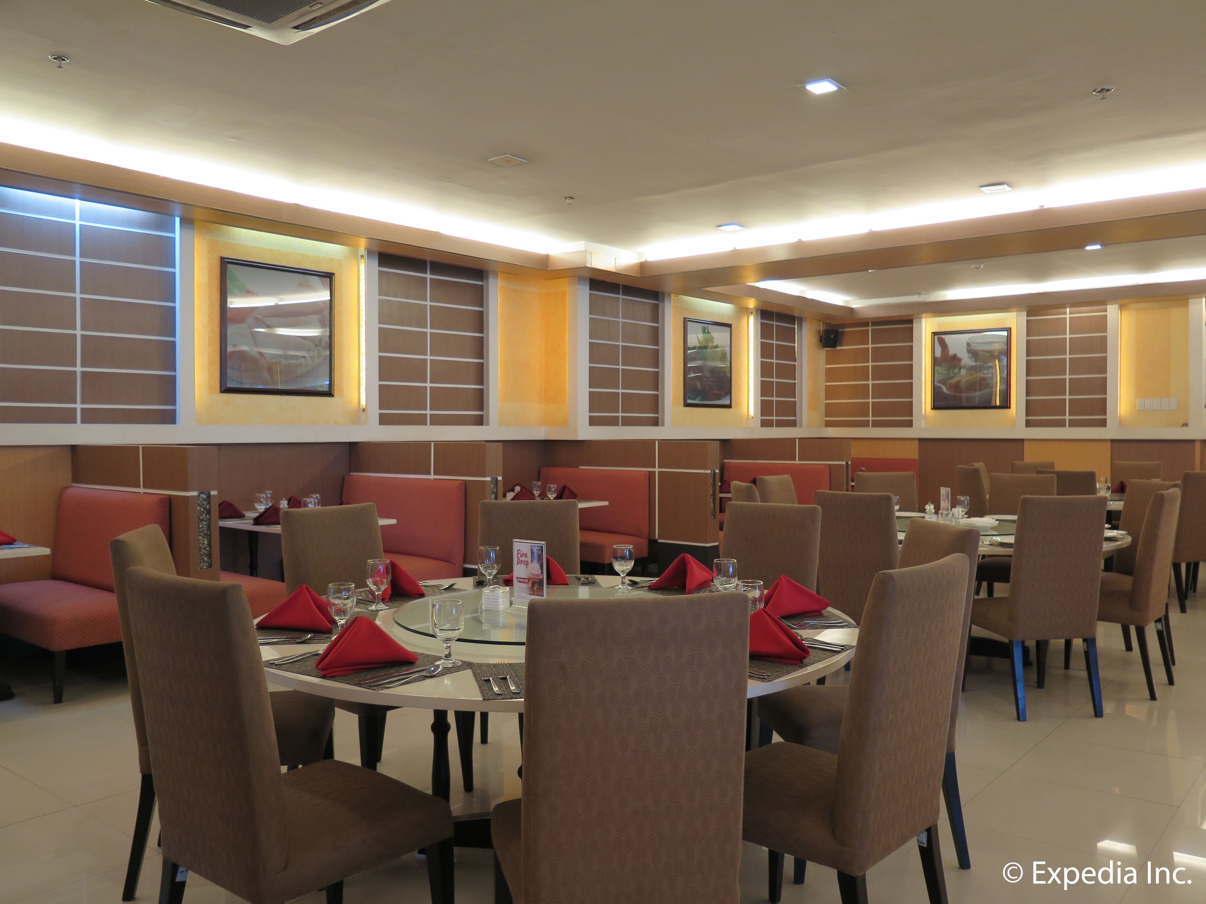 A restaurant with booths and round tables, each with red napkins and glasses.