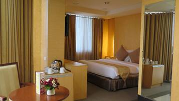 A hotel room with a bed, a desk with a telephone, a chair, a small table with a vase of flowers, and a mirror.
