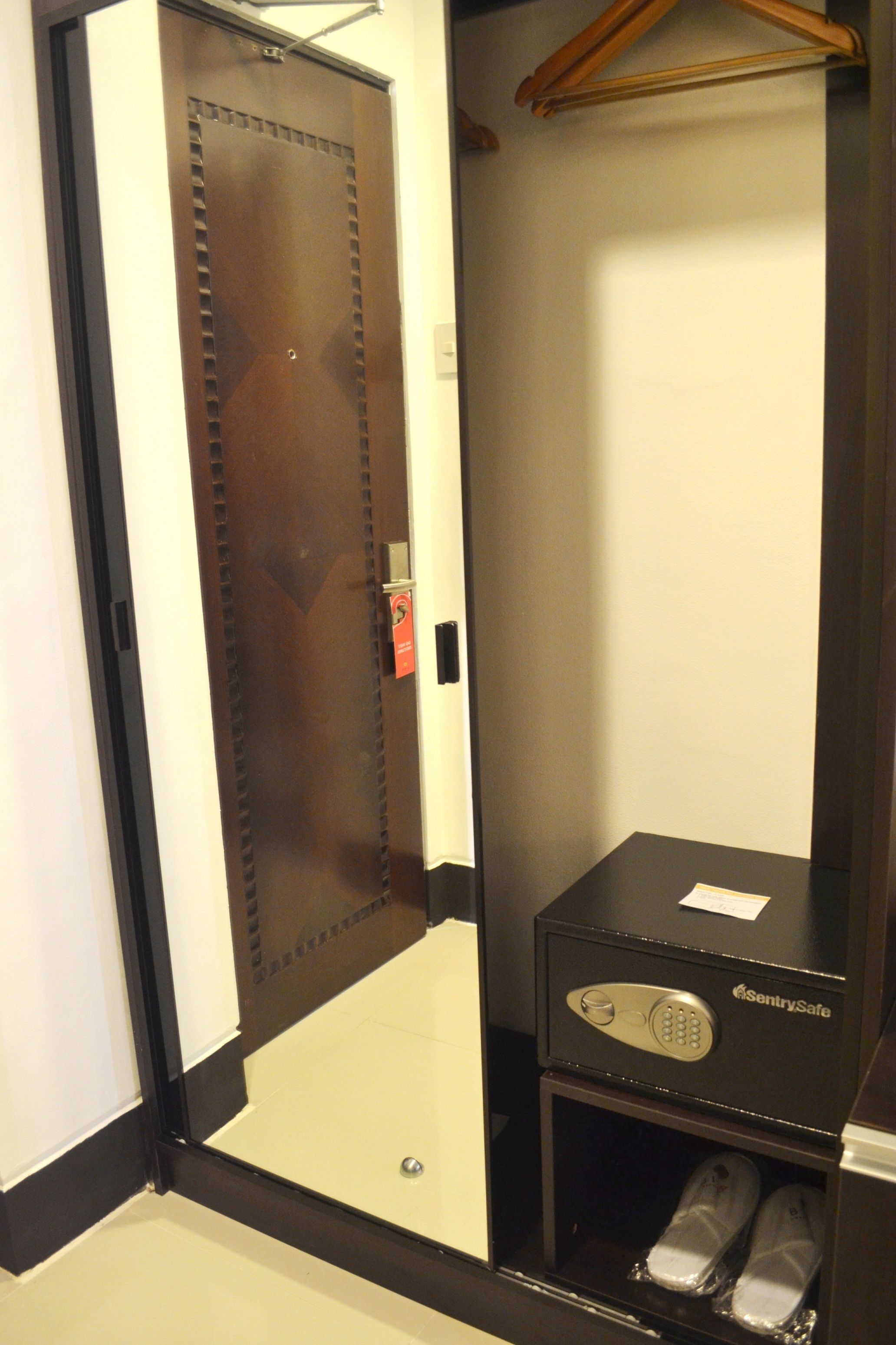 A hotel room with a wooden door, a shoe rack, and a safe.