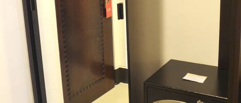 A hotel room with a wooden door, a shoe rack, and a safe.