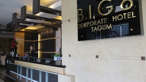 A reception desk at the BIG8 Corporate Hotel in Tagum with a modern design, a receptionist, and a digital clock displaying the time.