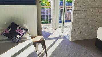 A room with a bed, a chair, and a view of a balcony with a wooden fence.