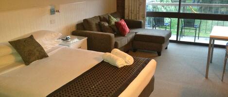 Quarto de hotel com uma cama grande, um sofá, um banquinho e uma mesa pequena.