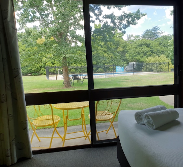 Habitación de hotel con un ventanal grande, una cama y una toalla blanca doblada con cuidado, con vistas a una piscina y una zona de estar al aire libre.