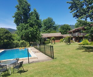 A backyard with a swimming pool, a fenced patio area, and a grassy lawn.