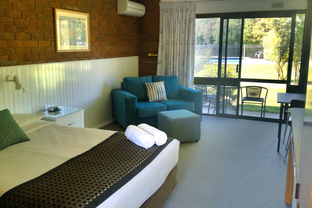 Habitación de hotel con cama, sofá azul, una mesita y vistas a una piscina y jardín.
