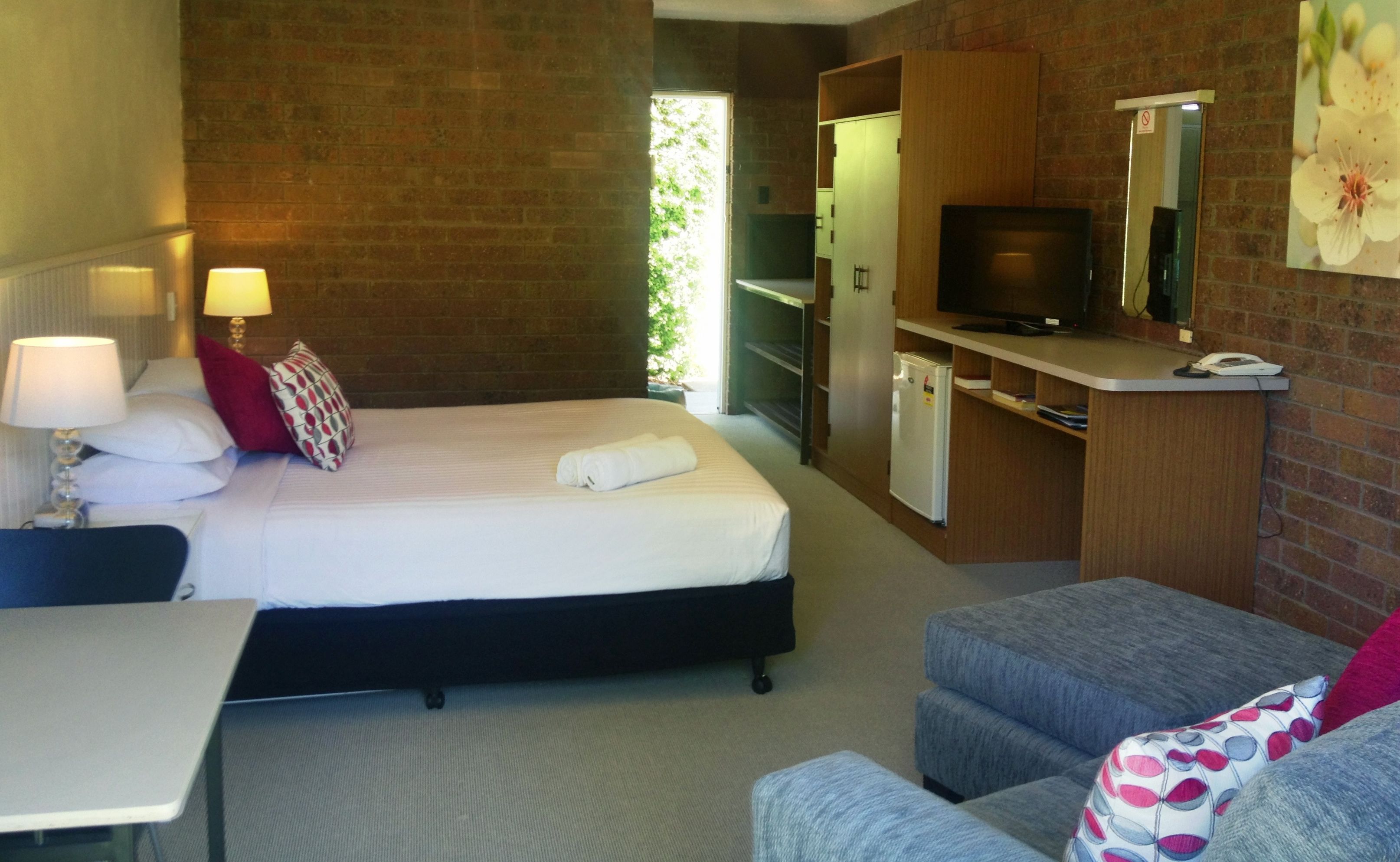 A hotel room with a bed, bedside lamps, a desk, a small kitchenette, a TV, and a seating area.