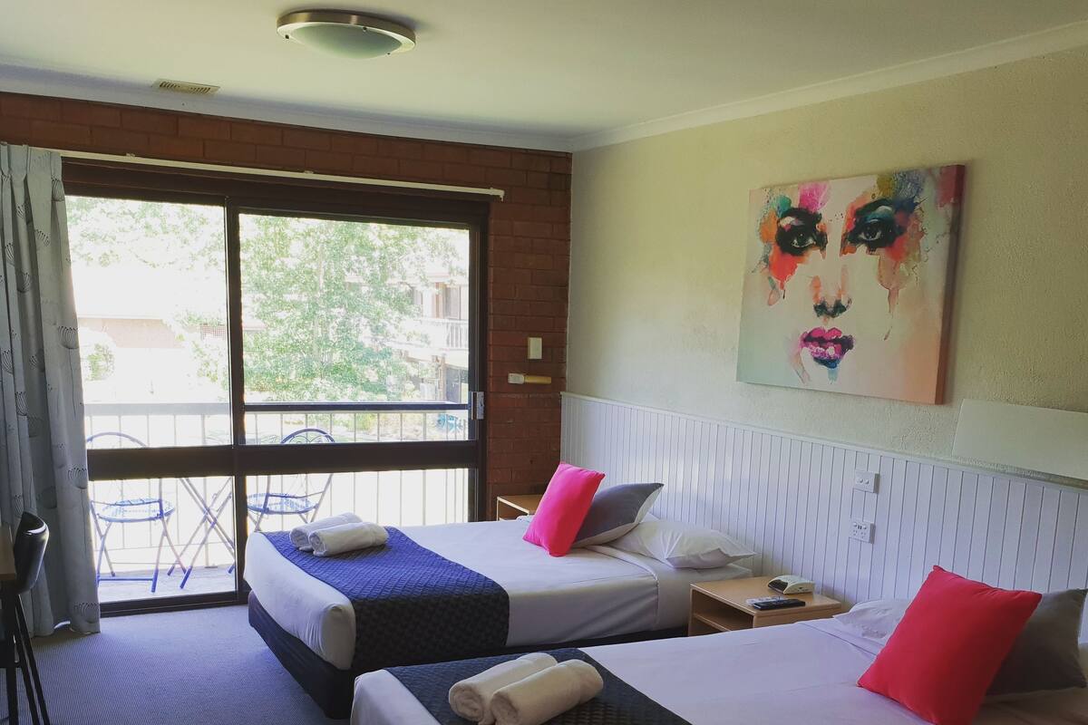 Habitación de hotel con dos camas, ventana que da al exterior, un cuadro en la pared y una mesita con un teléfono.