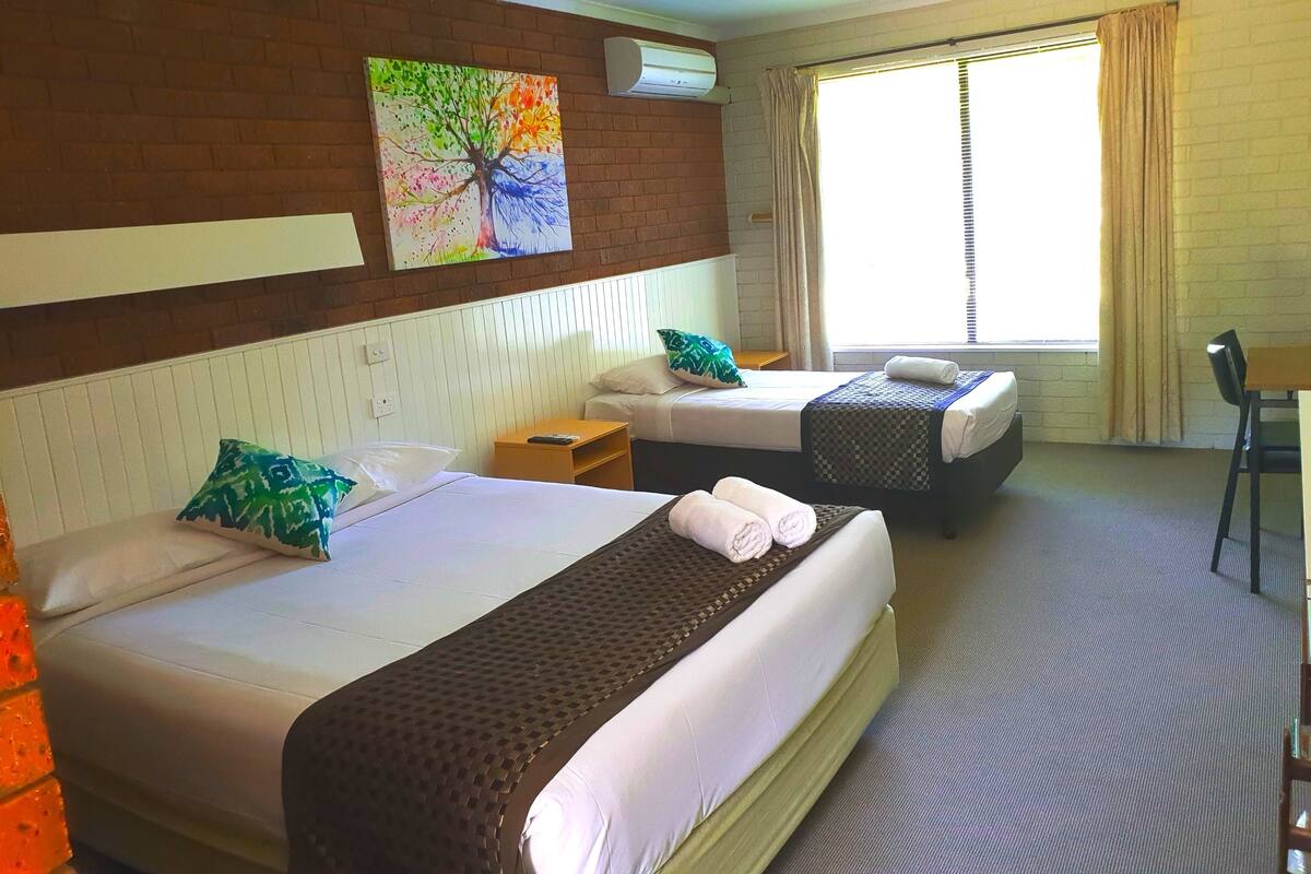 Habitación de hotel con dos camas, un cuadro en la pared, un equipo de aire acondicionado y una ventana con cortinas.