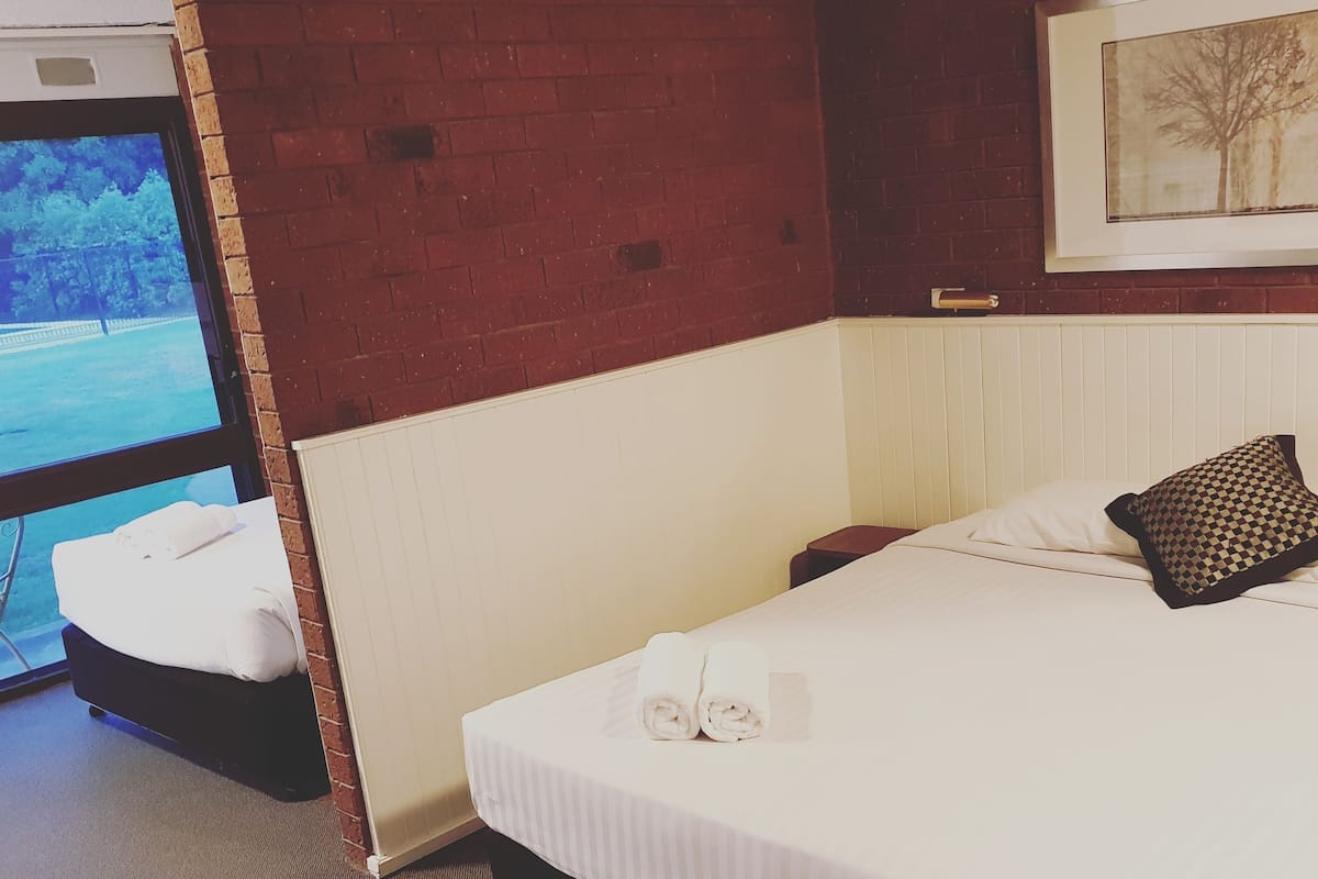 Habitación de hotel con cama, mesita de noche, ventana y un cuadro en la pared.