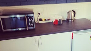 A kitchen with a microwave, kettle, and a coffee maker on the counter. - Motel Sierra (Bright)