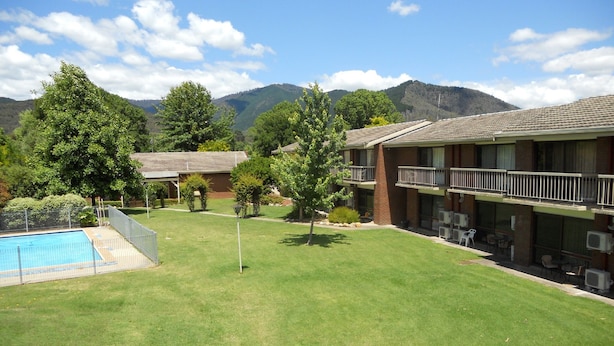 A hotel with a swimming pool, a well-maintained lawn, and a mountain backdrop. - Motel Sierra (Bright)