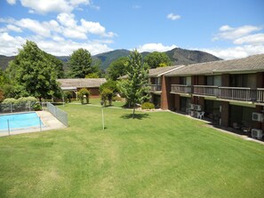 Un hotel con piscina, césped bien cuidado y montañas al fondo.