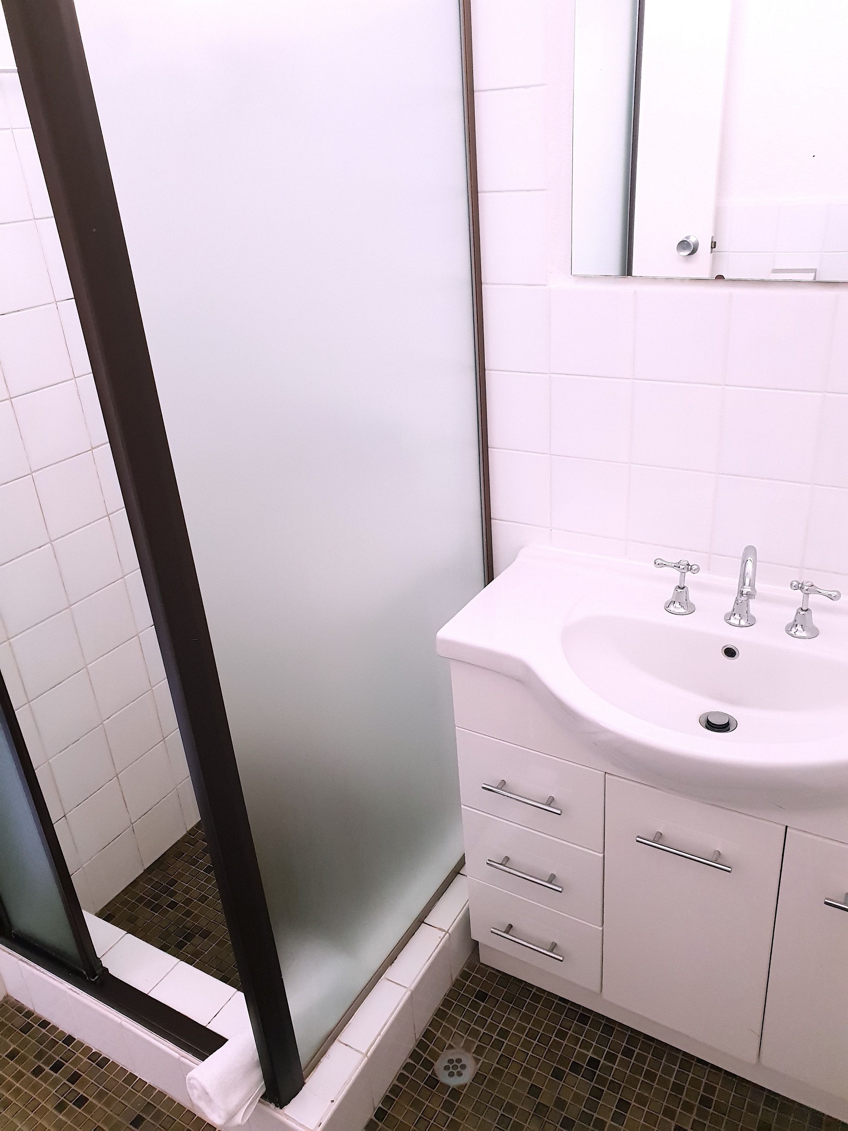 A bathroom with a white sink, two faucets, a mirror above the sink, and a shower area with a glass door.