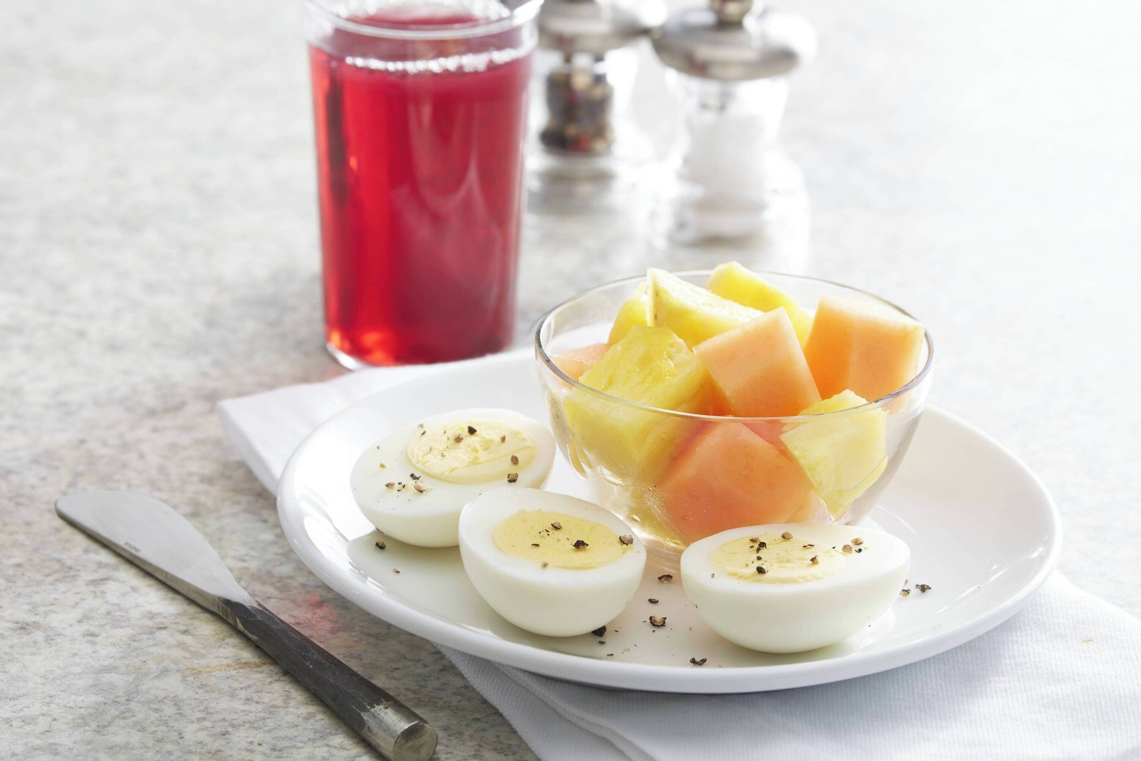 A plate with fruit and hard-boiled eggs, a knife, and a glass of red drink on a marble surface.