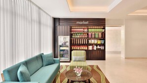 A modern interior with a teal sofa, a striped armchair, a glass coffee table with a vase, and a wall unit labeled 'market' with various food items. - Fairfield by Marriott Pune Kharadi (Pune)