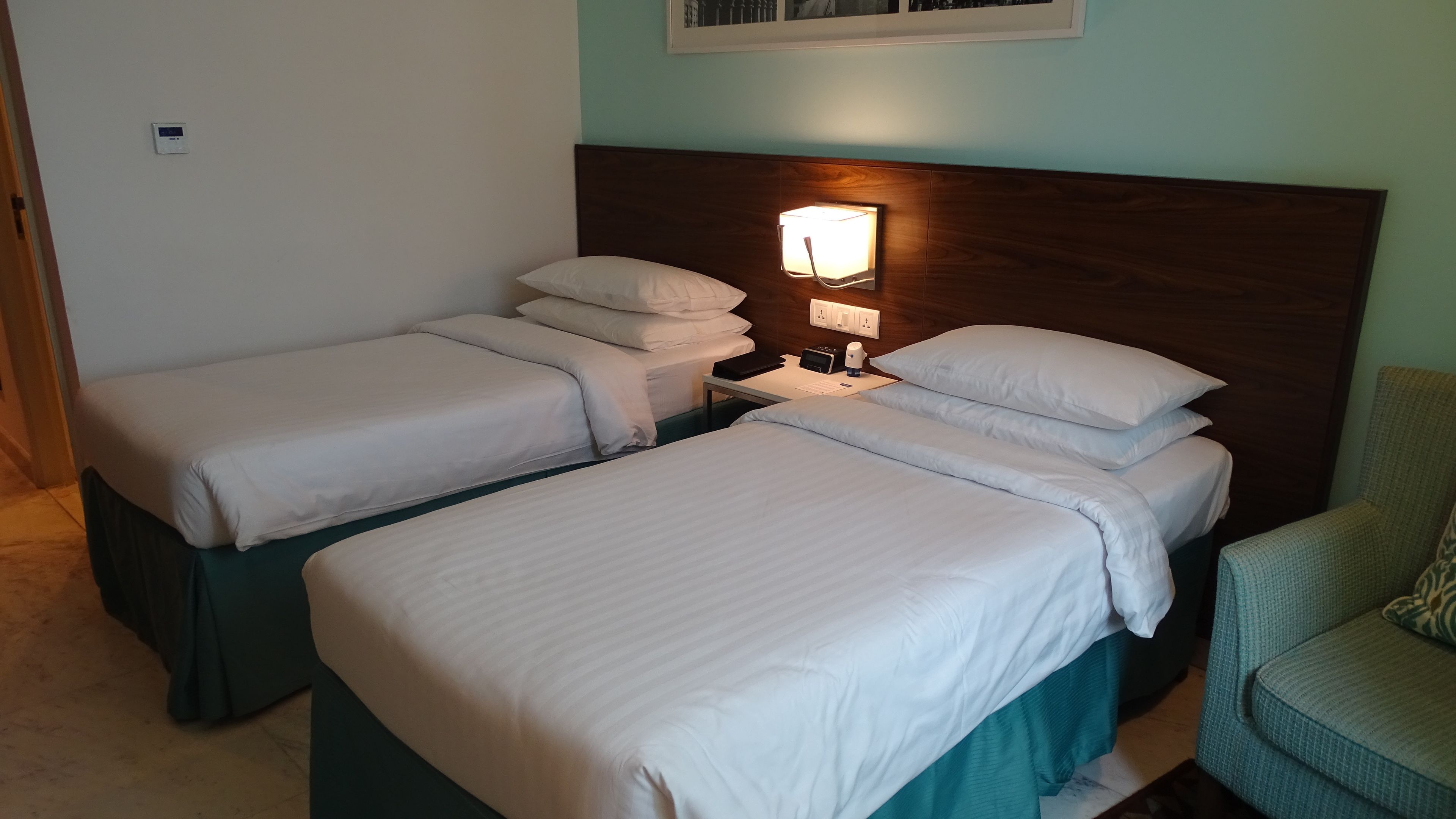 Una habitación de hotel con dos camas individuales, una mesita de noche con lámpara y una silla.