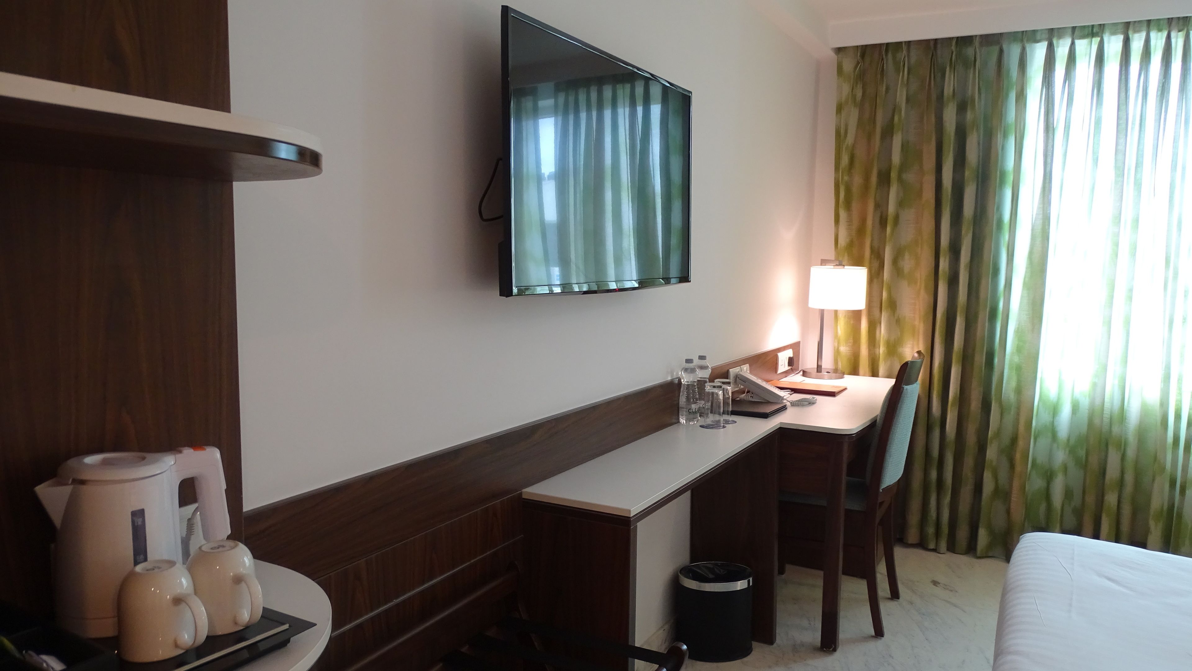 Habitación de hotel con escritorio, silla, cama, televisión y ventana con cortinas.