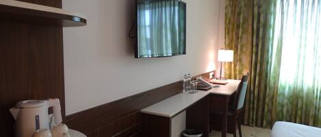 Habitación de hotel con escritorio, silla, cama, televisión y ventana con cortinas.