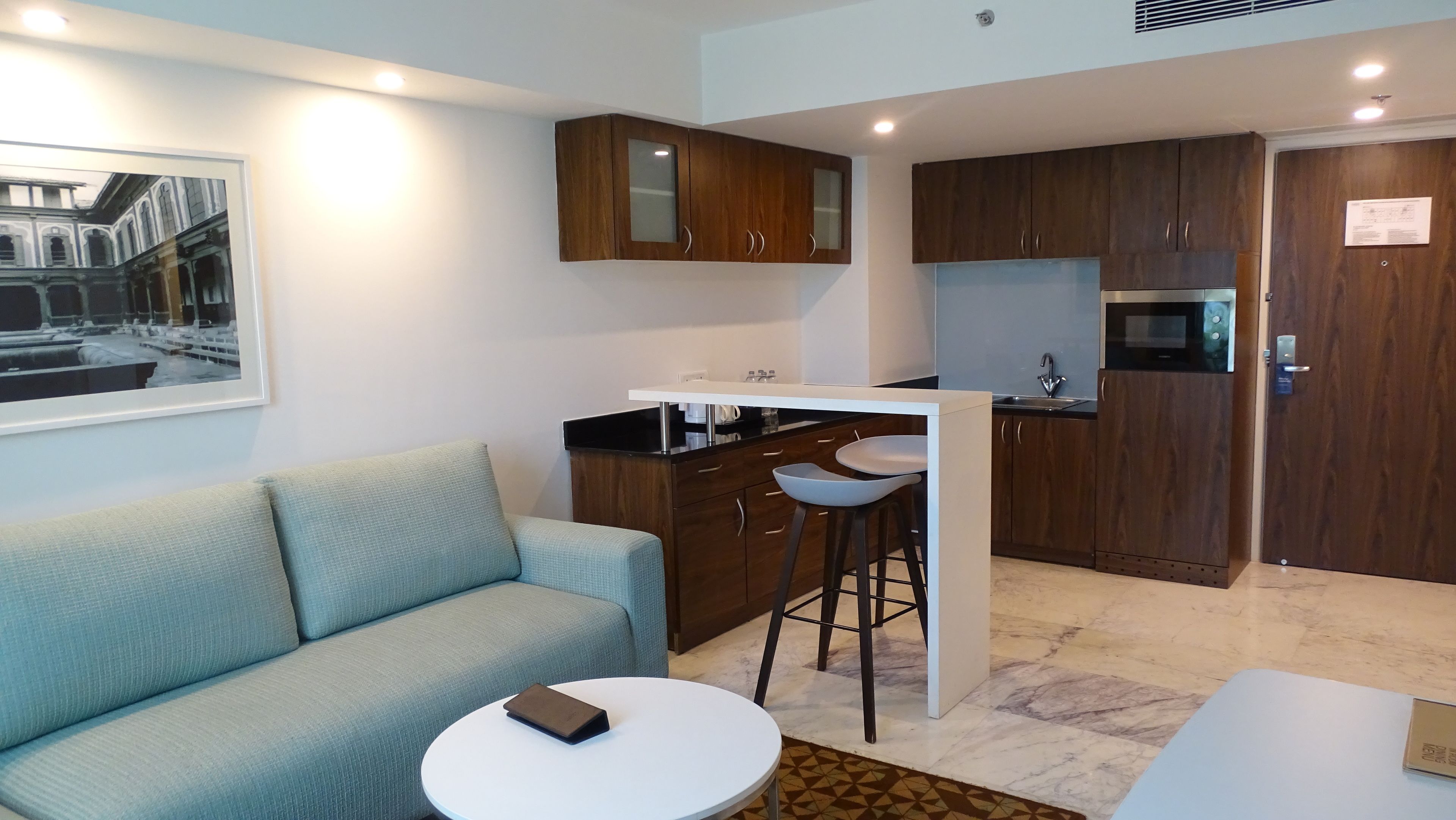 A modern apartment with a living area featuring a sofa and a round table, a kitchenette with wooden cabinets, and a dining area with a bar stool.