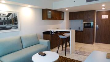 A modern apartment with a living area featuring a sofa and a round table, a kitchenette with wooden cabinets, and a dining area with a bar stool.