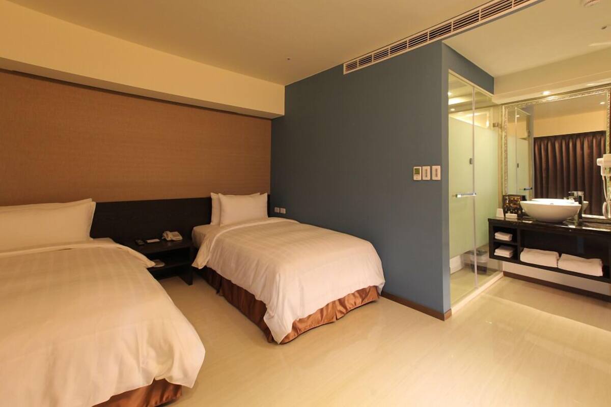 A hotel room with two beds, a bathroom with a large mirror, and a bedside table with a phone.