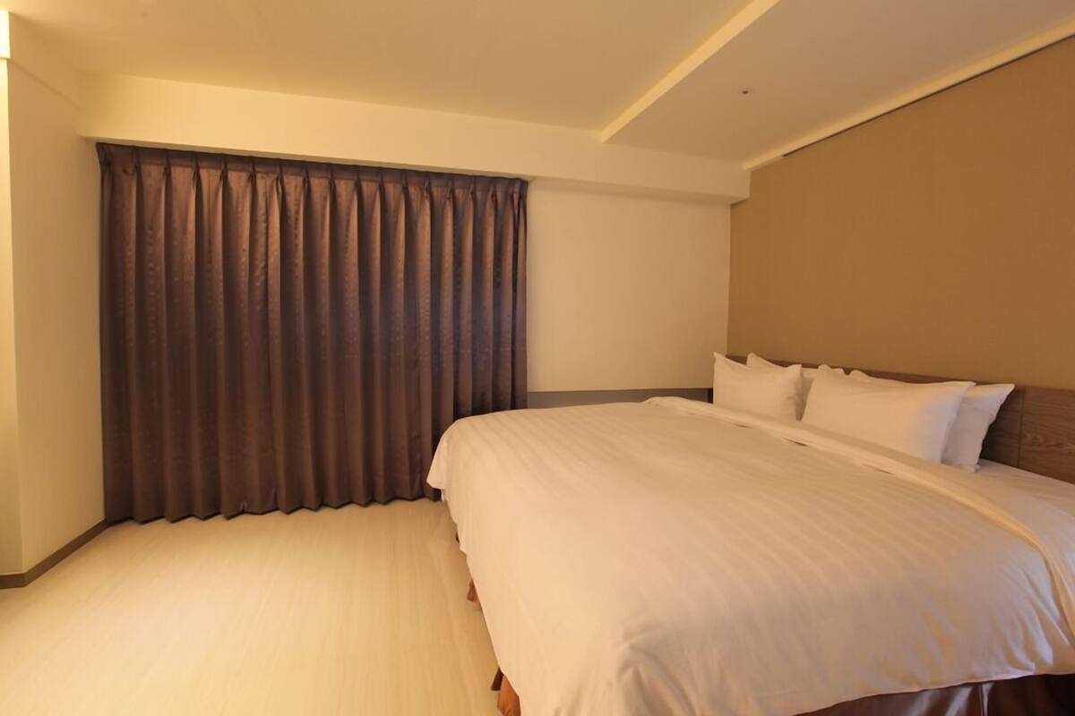 A hotel room with a large bed, a headboard, and a curtain.