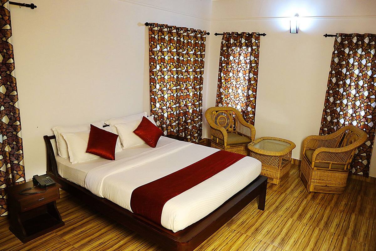A hotel room with a large bed, two wicker chairs, a small table, and a nightstand with a phone.