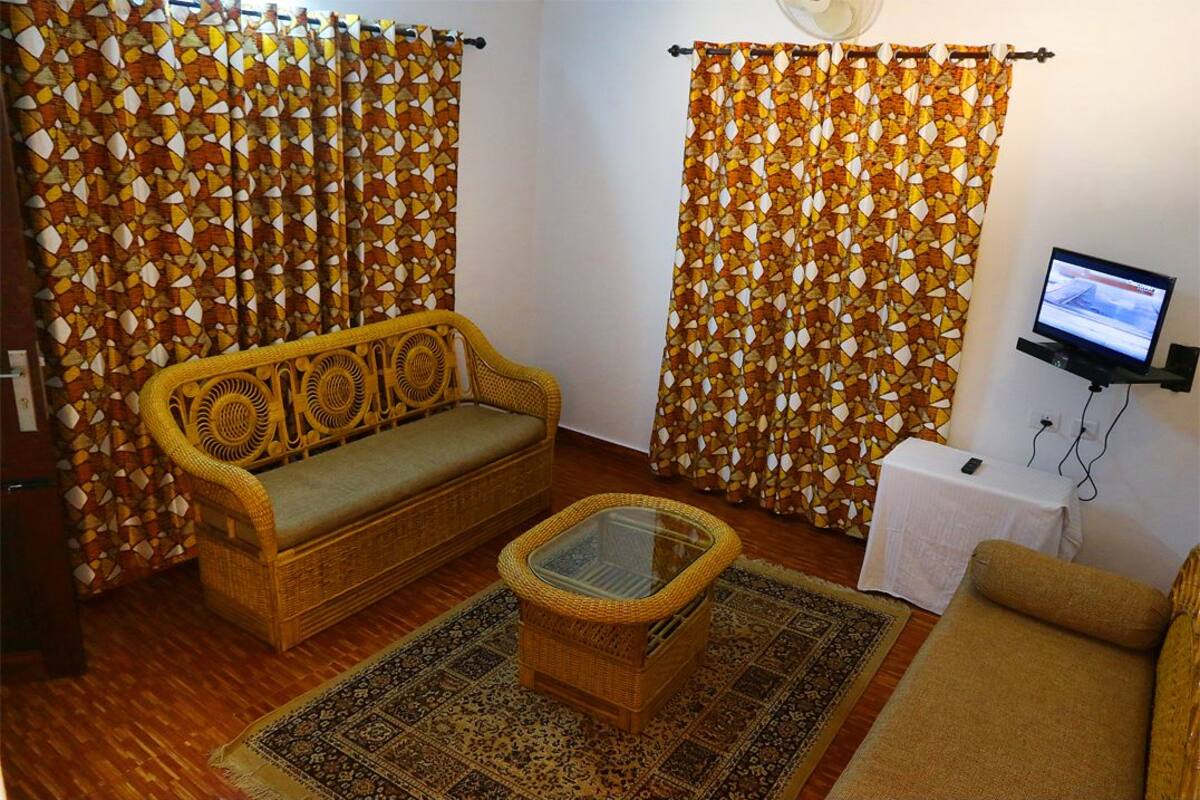 A living room with a sofa, a glass-top coffee table, a patterned rug, and curtains with a geometric design.