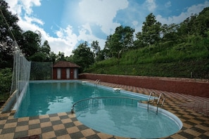 A swimming pool with a checkered floor, surrounded by a brick wall and a grassy hill. - Crescent Residency (Sulthan Bathery)