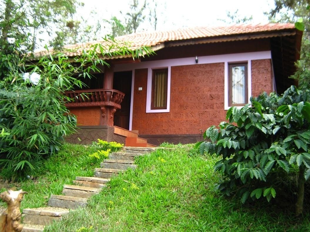 A rustic house with a red brick exterior, a wooden balcony, and a stone staircase leading to the entrance.