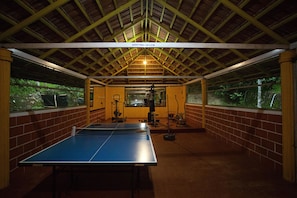 An indoor ping pong table with exercise equipment, a wooden ceiling, and brick walls. - Crescent Residency (Sulthan Bathery)