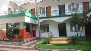 A two-story building with a green and white facade, a balcony with a metal railing, and a small garden area with a pool. - Raja Park Beach Resort (Varkala)