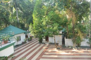 A courtyard with a tiled walkway, surrounded by lush greenery and a building with a green roof. - Raja Park Beach Resort (Varkala)