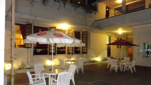 An outdoor patio area with white plastic chairs and tables, two umbrellas, and a brick wall. - Shalimar Hotel (Colombo)