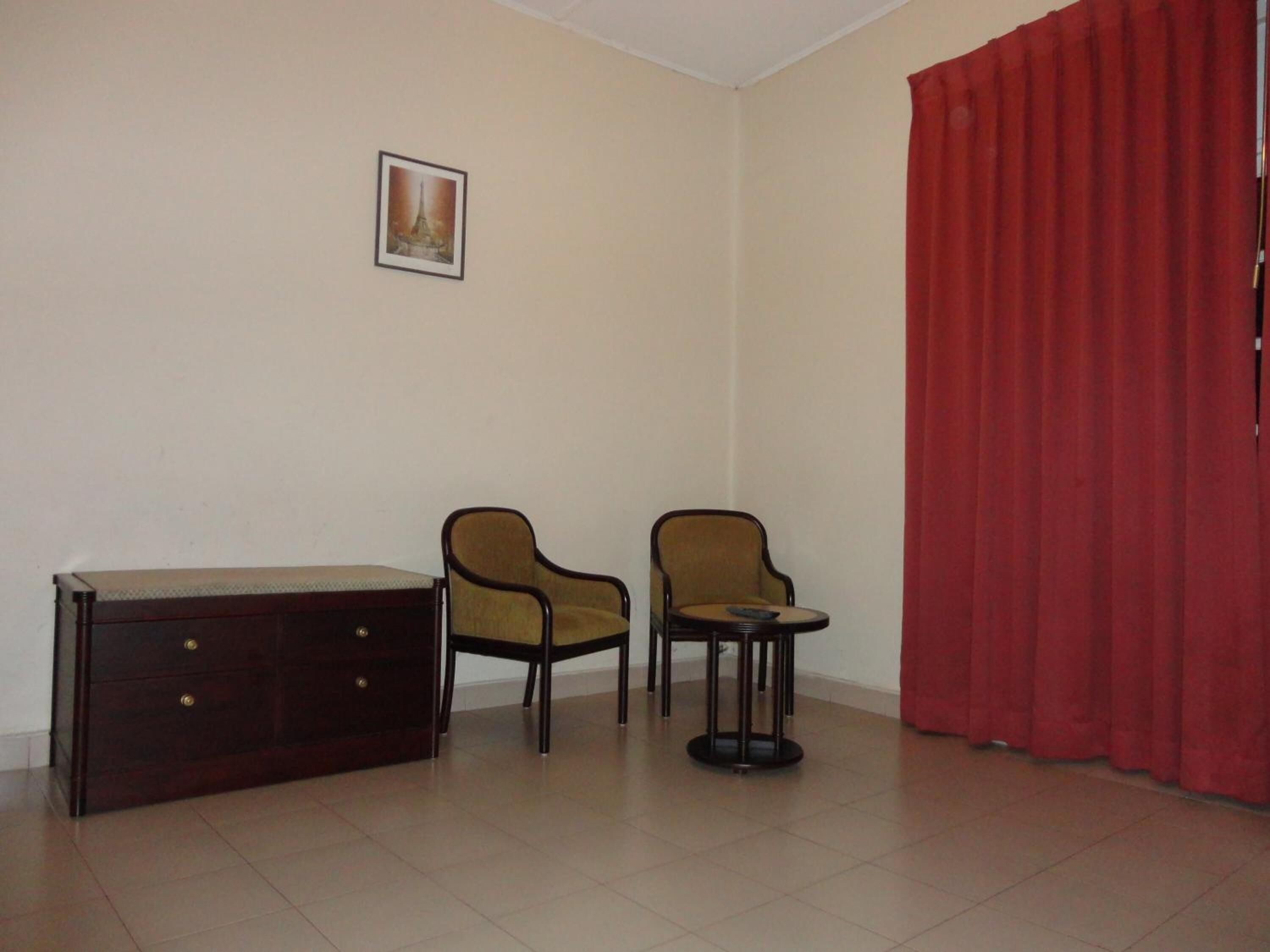Una habitación con un aparador de madera oscura, dos sillones, una mesita redonda y una cortina roja.
