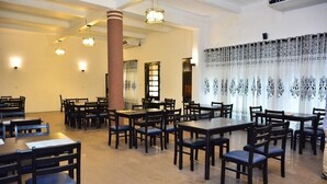 A spacious dining area with multiple tables and chairs, large windows with patterned curtains, and hanging pendant lights. - Shalimar Hotel (Colombo)