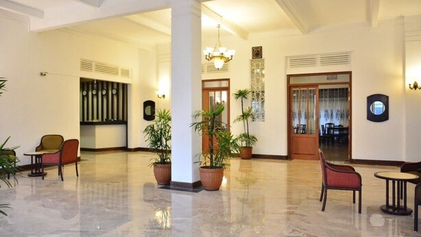A spacious lobby with a polished marble floor, several potted plants, and a mix of seating options including chairs and a small table. - Shalimar Hotel (Colombo)