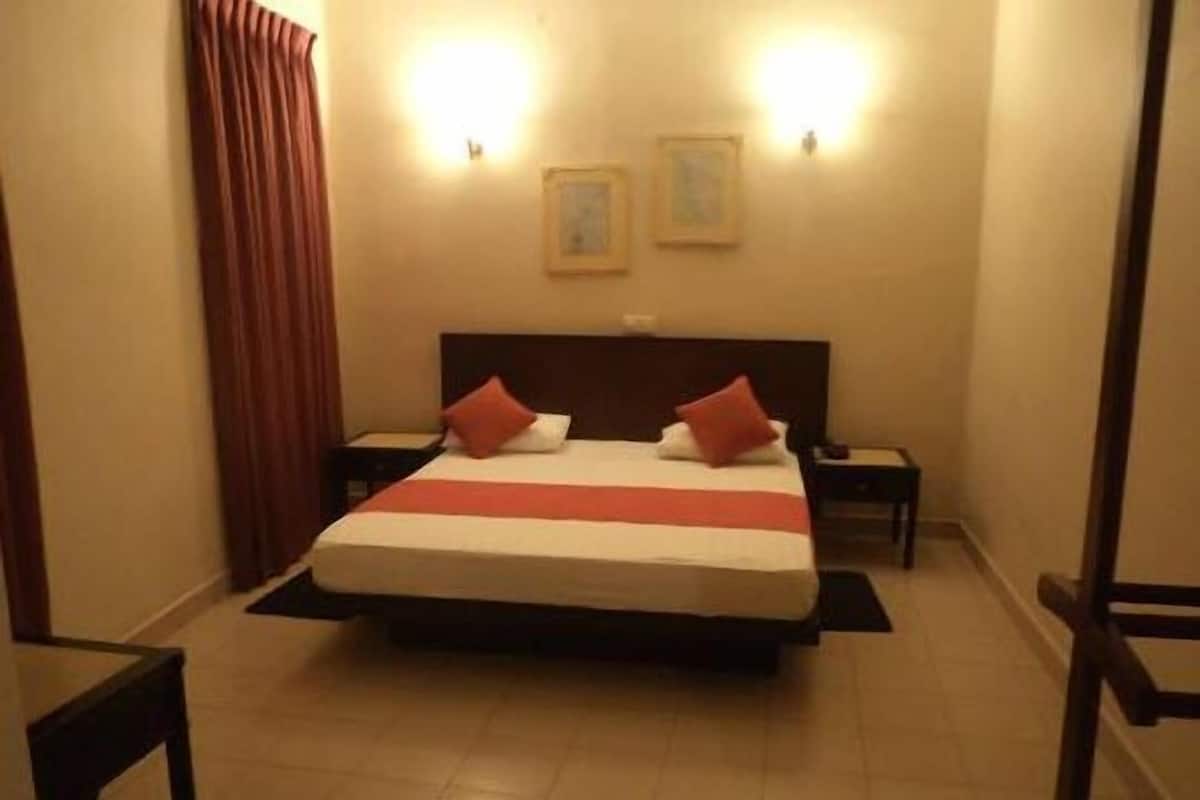 A hotel room with a large bed, two bedside tables, a headboard, and two wall-mounted light fixtures.