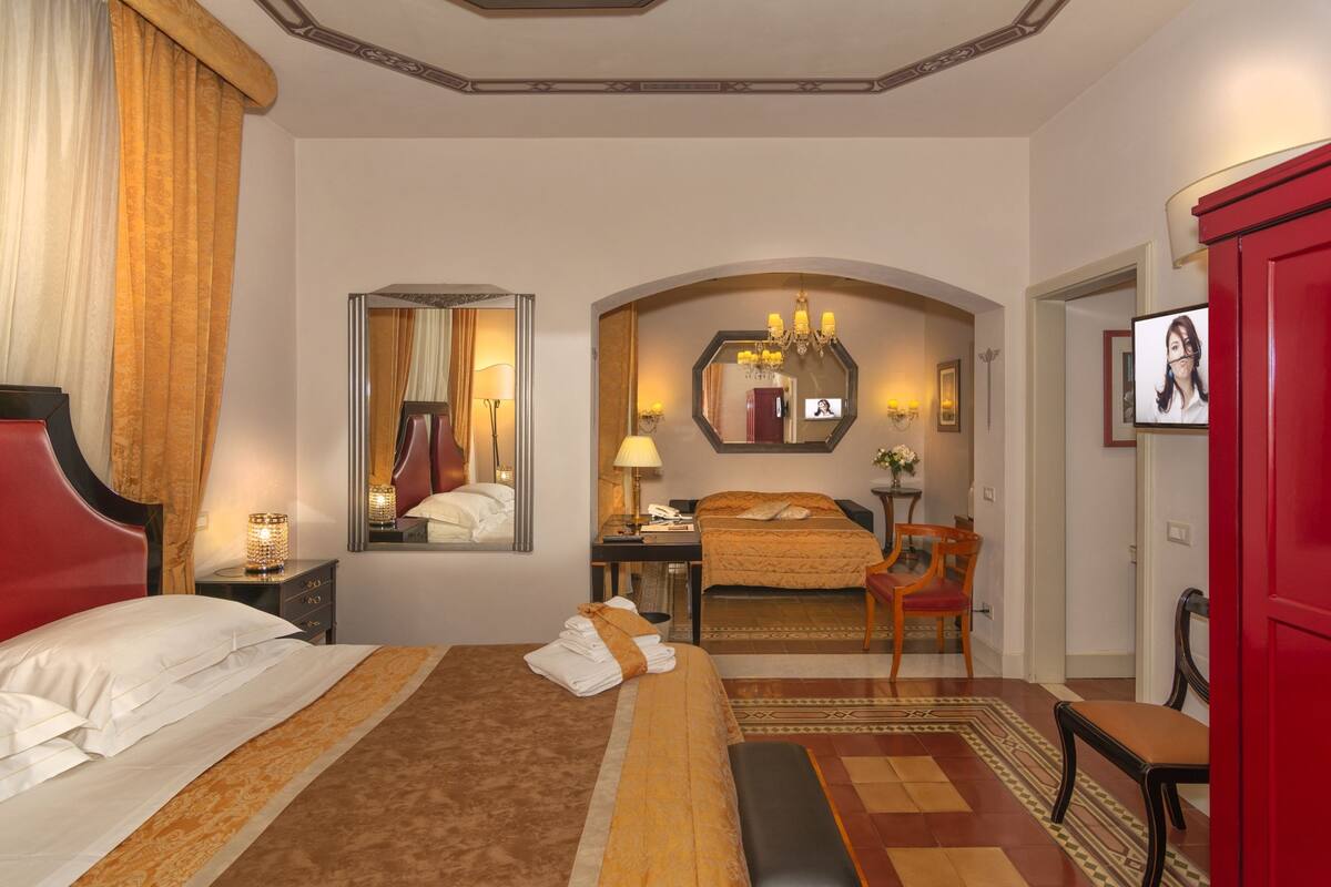 A hotel room with a large bed, a desk with a lamp, a mirror, and a television.