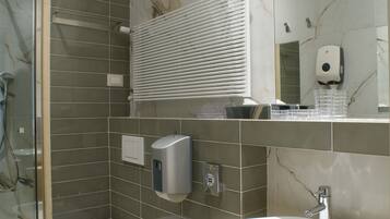 Un baño moderno con cabina de ducha de vidrio, dos bidés, un lavamanos y un espejo con dispensador de jabón.