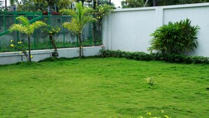 A well-maintained grassy lawn with a white wall and a green fence in the background. - Cosy Regency (Ambalapuzha)
