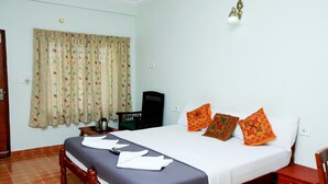 A neatly made bed with a blanket and towels, a bedside table with a kettle, and a window with curtains. - Cosy Regency (Ambalapuzha)